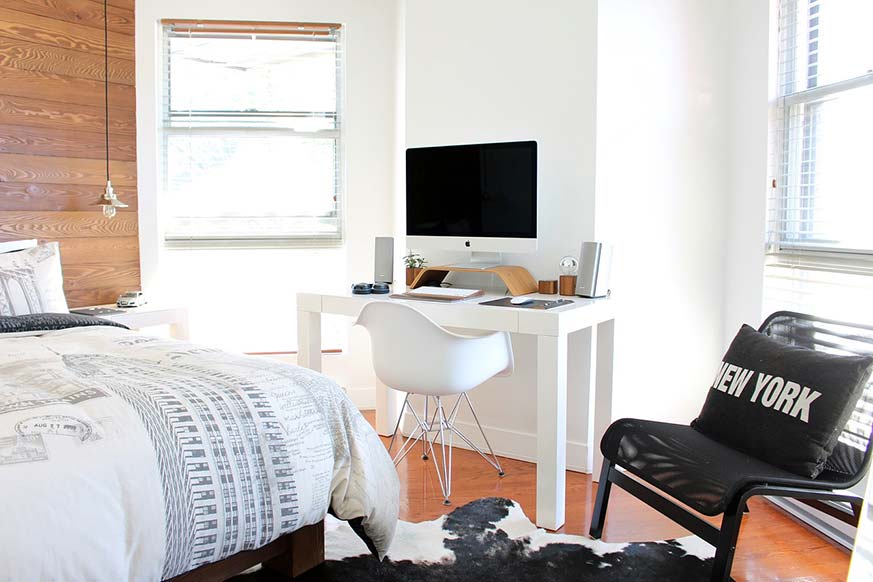Dormitorio juvenil con un escritorio blanco en el centro de la imagen, una cama en la derecha y una silla en la parte izquierda de color negro.
