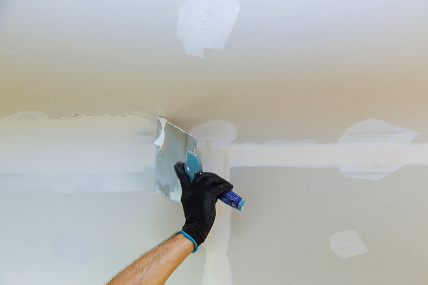 En la imagen aparece una mano aplicando pintura antigoteras en el techo