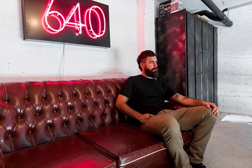 colocar cuadros encima del sofá: hombre sentado en un sofa de cuero con un cuadro led rojo del número 640 sobre la cabeza.