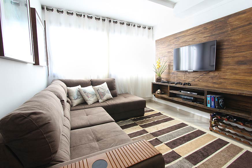 salón en tonos marrones. El sofá tiene forma de L y en la pared de enfrente encontramos una modulo flotante en tono madera con una tv de pantalla plana encima.
